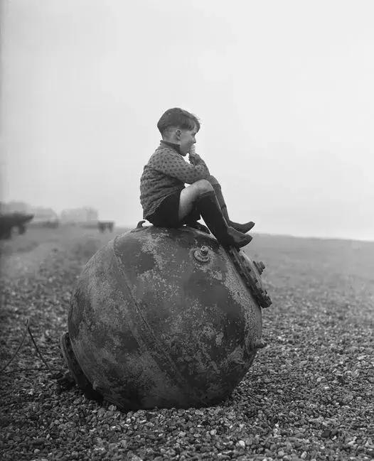 1945年,英国肯特海滩上的一个小男孩坐在被冲上海滩的水雷上吃着